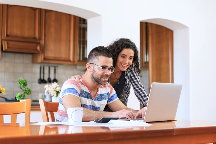 a happy couple searching a house online using their laptop